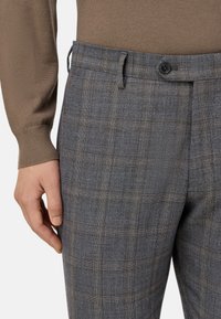 Pantalones de cuadros grises con una textura sutil, con cierre de botón y bolsillos laterales, combinados con un suéter marrón suave.