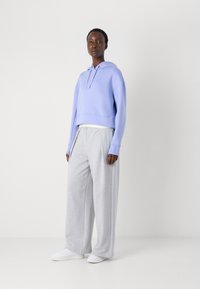 Haut de survêtement court violet clair avec capuche, associé à un pantalon de survêtement gris ample et des baskets blanches, mettant en avant un style décontracté et détendu.