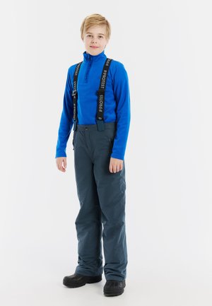 Blauwe fleece pullover met een halflange ritssluiting, gecombineerd met grijze sneeuwbroek met verstelbare zwarte schouderbanden en zwarte waterdichte laarzen.