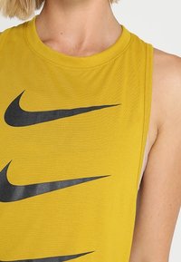 Canotta atletica gialla senza maniche realizzata in tessuto strutturato, caratterizzata da numerosi loghi swoosh neri della Nike sul davanti.