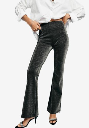High-waisted flared pants in black with a shimmering finish. Features a smooth texture and a fitted silhouette with a subtle zipper detail at the hem.