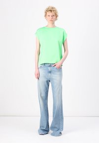 Haut vert à manches courtes avec une coupe décontractée, associé à un jean en denim large bleu clair. Texture lisse, design simple, sans motifs ni accents.