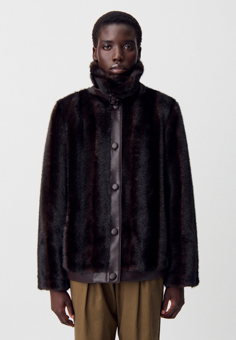 Chaqueta de piel sintética marrón con collar alto, frente de cuero marrón en contraste, botones a presión y un corte relajado, que muestra una superficie suave y texturizada.