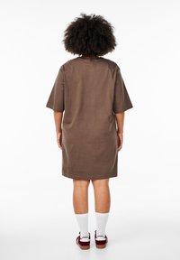 Brun bomull t-shirtklänning med korta ärmar, rak passform och rund halsringning. Bärs med vita strumpor och vinröda skor.