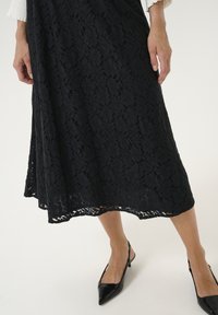 Juoda nėriniuota suknelė su gėlių raštu, iki kelių ilgis ir banguoti kraštai. Sukomplektuota su juodais aštriais slingback bateliais.