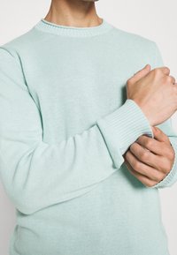 Maglioncino verde menta chiaro con scollo rotondo, polsini a costine e lavorazione a maglia testurizzata. Il tessuto è morbido e leggero.