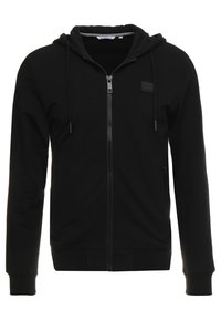 Sudadera con cremallera negra, capucha con cordón, bolsillos laterales, tejido texturizado y un pequeño logo en el pecho.