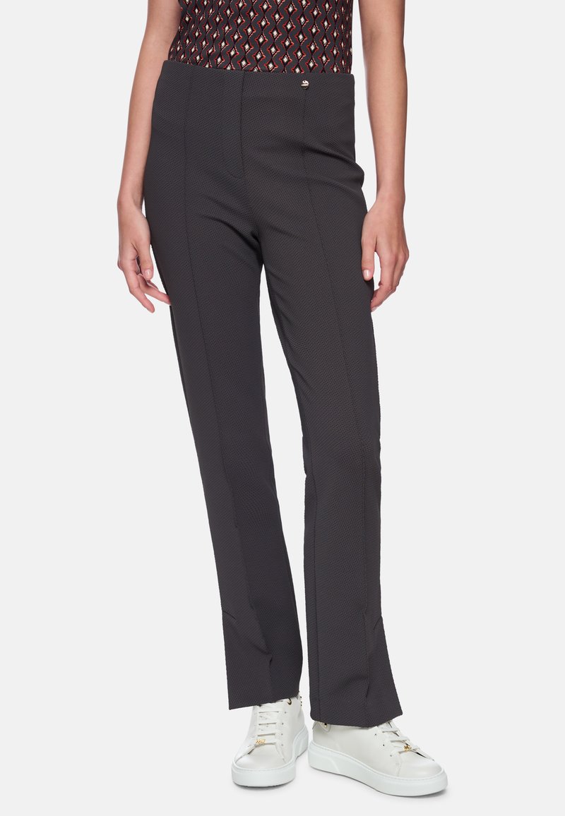 Schwarze gemusterte Hose mit enger Passform, glatter Textur und maßgeschneidertem Schnitt, kombiniert mit weißen Sneakers.