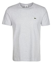 T-shirt en coton gris à manches courtes et col rond, avec un petit logo vert Lacoste sur la poitrine. Tissu doux et texturé.