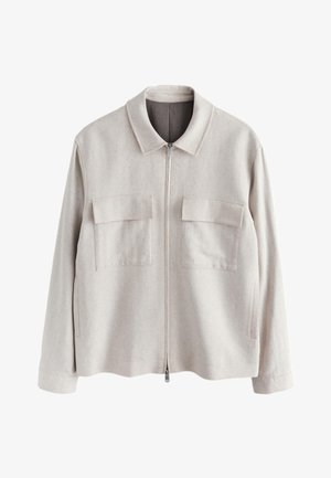 Lyse beige jakke med lynlås og lange ærmer, to brystlommer med klap og en spids krave, vist på hvid baggrund.