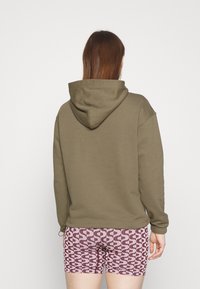 Sudadera capucha verde olivo con un corte holgado, combinada con pantalones cortos rosas estampados que presentan un diseño ondulado. Tejido suave, detalles mínimos.
