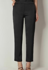 Pantalons noirs ajustés avec une texture lisse et mate. Dotés d'une taille élastique mi-haute et d'une coupe slim, arrivant à la cheville avec un ourlet net.