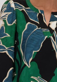 Korte mouwen top met een zwarte achtergrond versierd met grote groene en blauwe bladpatronen; V-hals ontwerp met een effen groene bies.