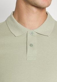 Lichtgroen polo shirt van een gestructureerde stof, met een klassieke kraag en een twee-knopen sluiting. Bevat subtiele stikdetails.