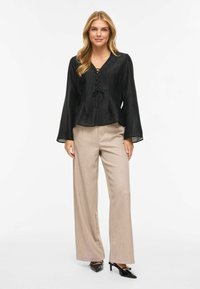 Svart bluse med lange ermer og snøring foran, kombinert med beige høytlivede bukser med vide ben og svarte sko med hæl.
