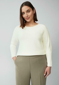 Gebreide crème trui met ribbeltextuur, ronde halslijn en lange mouwen, gecombineerd met hooggesneden olijfgroene broek.
