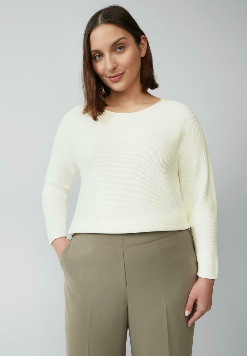 Gebreide crème trui met ribbeltextuur, ronde halslijn en lange mouwen, gecombineerd met hooggesneden olijfgroene broek.