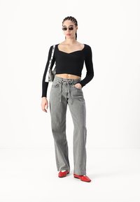 Top corto de manga larga negro con canalé, pantalones de pierna ancha grises de cintura alta y zapatos rojos de punta. Modelo llevando gafas de sol pequeñas y bolso plateado.