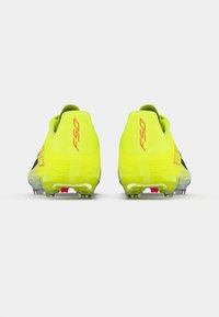 Λαμπερά κίτρινα ποδοσφαιρικά παπούτσια με υφή από συνθετικό υλικό, μαύρες λεπτομέρειες και διαφανή σόλα με τακάκια για πρόσφυση. Μοντέλο F50.