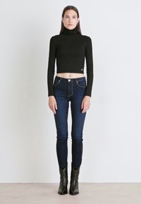 Čierny priliehavý rolák s krokom spárovaný s tmavomodrými skinny džínsami. Modelka má na sebe čierne členkové čižmy a stojí na svetlom pozadí.