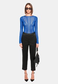 Blauwe doorschijnende body met lange mouwen en een aansluitend ontwerp, gecombineerd met zwarte tailored broek, zwarte hakken en een zwarte handtas.