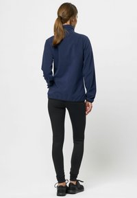 Marinblå fleecepullover med ståkrage och långa ärmar, i kombination med svarta leggings och svarta träningsskor. Slät textur.