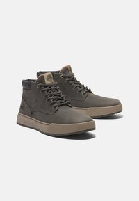 Dunkelgraue Lederstiefel bis zum Knöchel mit Gummisohle, runder Zehenform und kontrastierenden tanfarbenen Akzenten am Kragen und Logo. Metallische Ösen und Schnürsenkel.