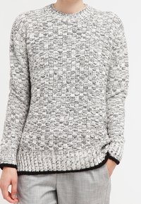 Grå och vit texturerad stickad tröja med rund halsringning, med kontrasterande mörka ribbade muddar och fåll, samt en avslappnad passform.
