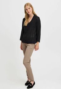 Pull en tricot noir avec un col en V et une coupe décontractée, associé à un pantalon slim beige et des mocassins noirs avec un accent doré.