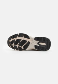 Semelle de chaussure avec un motif de bande de roulement en caoutchouc noir, présentant une semelle intermédiaire beige et crème. Surface texturée avec rainures et motifs d'adhérence.