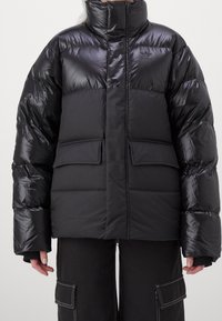 Black puffer jacket with a high collar, quilted texture, patch pockets, and a glossy finish. Features an adidas logo on the upper left.