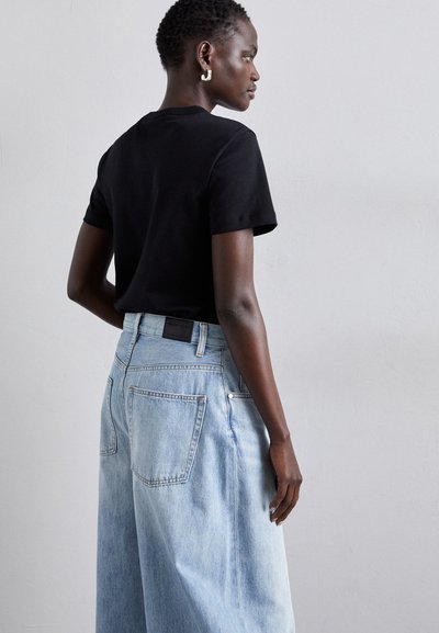 Μαύρο κοντομάνικο t-shirt συνδυασμένο με ανοιχτό μπλε ψηλόμεσο παντελόνι με φαρδιά πόδια. Το παντελόνι διαθέτει πίσω τσέπες και δερμάτινη ετικέτα στη μέση.