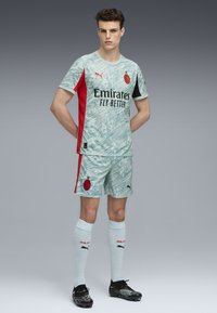 Maglia da calcio azzurro chiaro con motivo e dettagli rossi e neri, pantaloni abbinati e calzini bianchi. Presenta il logo Puma e la scritta "Emirates Fly Better".
