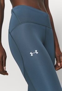 Legginsy z wysokim stanem, dopasowane, w ciemnoniebieskim kolorze z gładkiego materiału. Posiadają kontrastowe, białe logo marki oraz szczegółowe szwy.