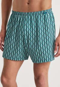 Mannenboxers van lichtgewicht stof, met een geometrisch patroon in teal en marineblauw, een elastische tailleband en een ontspannen pasvorm.
