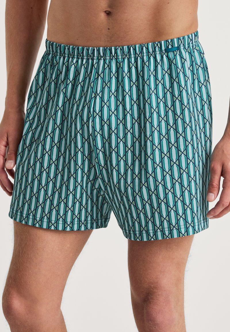 Mannenboxers van lichtgewicht stof, met een geometrisch patroon in teal en marineblauw, een elastische tailleband en een ontspannen pasvorm.