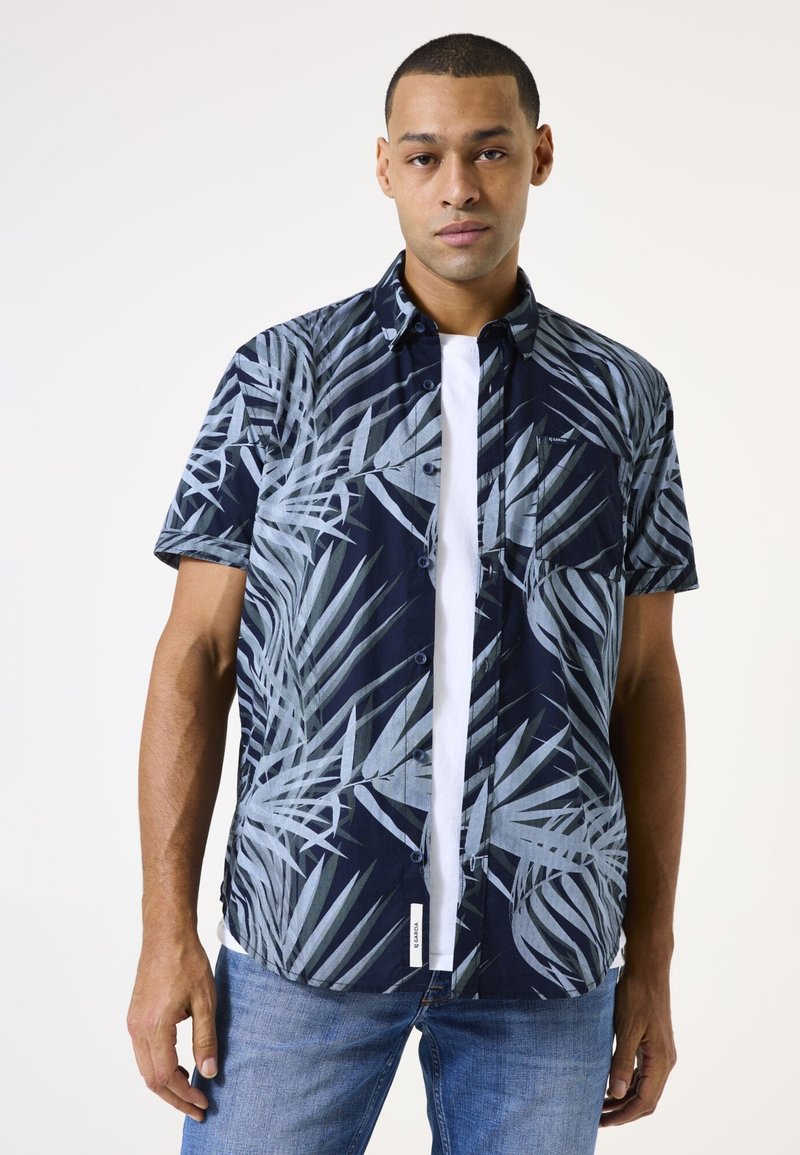 Camisa de manga corta abotonada en color navy con un patrón de hojas de palma en tonos de gris. Diseñada con un bolsillo en el pecho y una camiseta blanca visible.