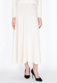 Jupe longue blanche en tissu doux, avec une texture lisse et un design évasé, légèrement brillante ; assortie à des chaussures à talons hauts noires.