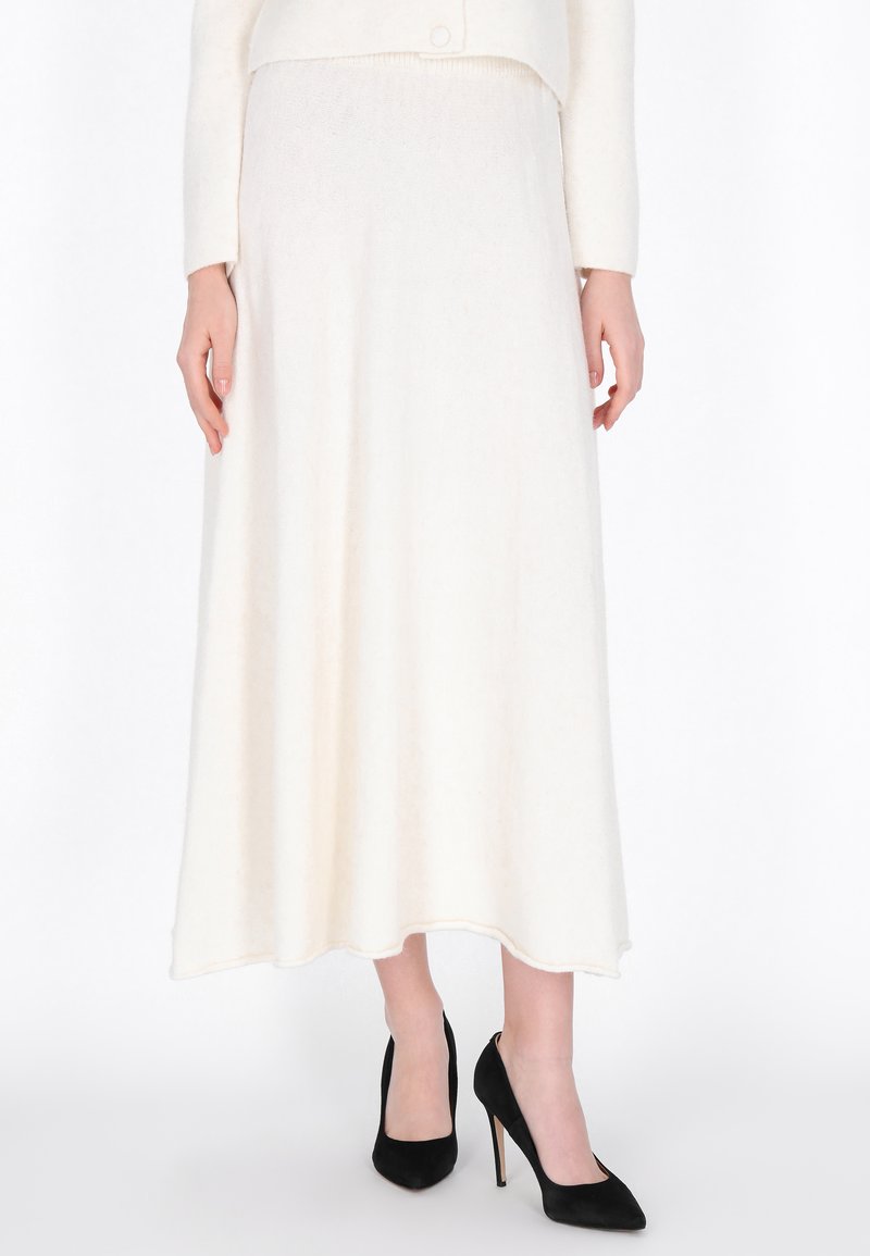 Jupe longue blanche en tissu doux, avec une texture lisse et un design évasé, légèrement brillante ; assortie à des chaussures à talons hauts noires.