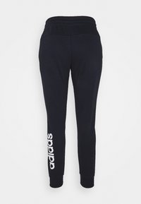 Pantalones de chándal negros con cinturilla acanalada, puños ajustados y logo de Adidas blanco impreso en la pierna izquierda. Textura de tela suave.