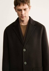 Cappotto in lana marrone scuro con rever a punta, due bottoni e tasche laterali. Tessuto morbido e design su misura per una vestibilità strutturata.