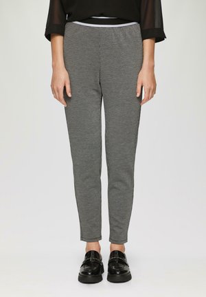 Un pantalon slim gris à carreaux avec une taille élastique noire, une texture lisse et une silhouette ajustée, associé à des chaussures noires brillantes.