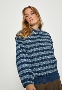 Niebieska pikowana kurtka w kratkę z teksturowanym wzorem. Posiada zamek błyskawiczny z przodu oraz kontrastowy deninowy pas na dole. W komplecie długie rękawy.