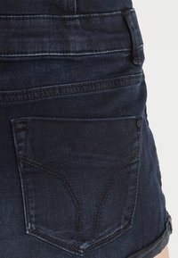 Tmavě modré denimové šortky s přiléhavým střihem, mají zadní kapsy, tónové prošívání a hladkou texturu s minimálním blednutím.