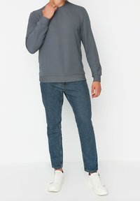 Sudadera gris acanalada con cuello redondo, usada con vaqueros azules y zapatillas blancas. Diseño sencillo, mangas largas y ajuste entallado.