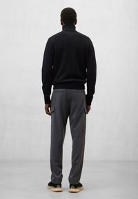 Dunkelgrauer Pullover mit hohem Kragen, kombiniert mit grauen Cargo-Hosen mit Seitentaschen. Getragen mit schwarzen Schuhen, vor einem hellen Hintergrund.