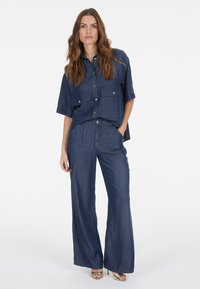 Denim two-piece outfit featuring a cropped button-up shirt with large pockets and wide-leg pants, both in a uniform dark blue shade.