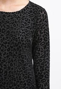 Svart sammetstop med rund halsringning och lång ärm, prytt med en texturerad leopardmönster.