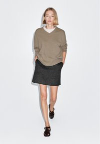 Maglione beige lavorato a maglia con scollo a v, gonna grigia scura con taglio dritto e sandali marroni con cinturini, con una texture liscia in tutto il capo.
