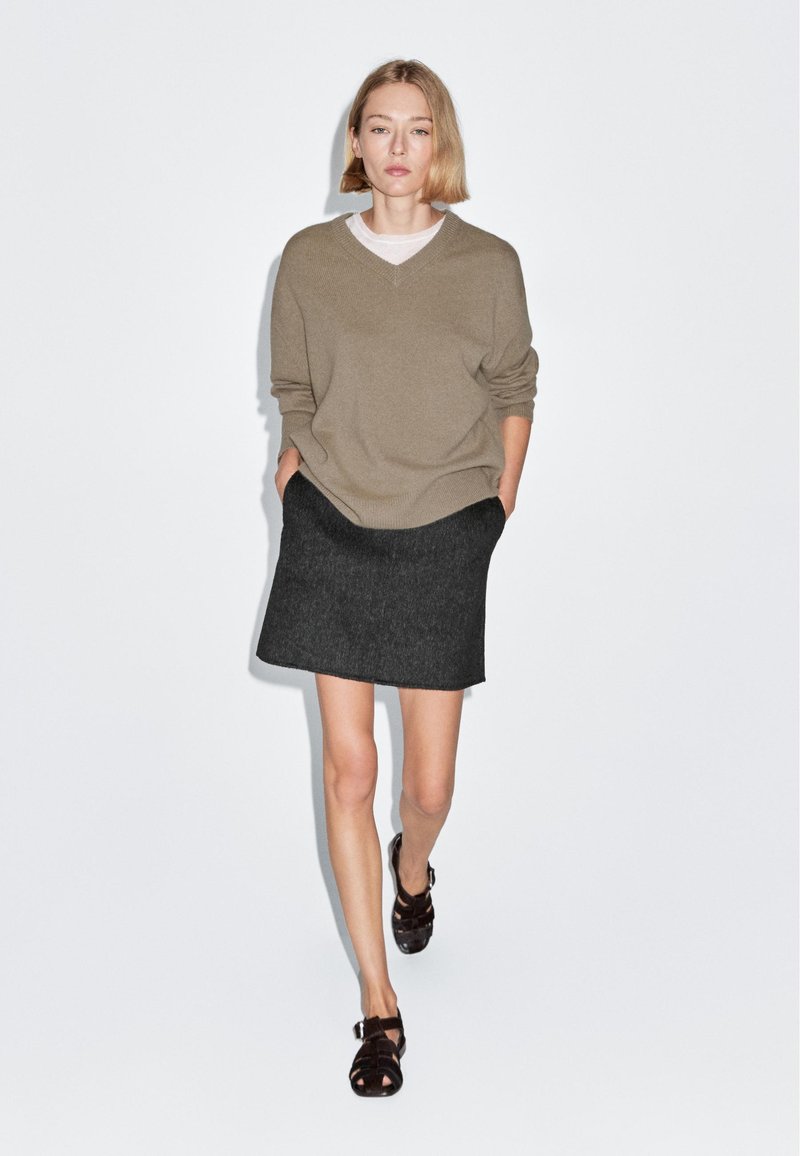 Maglione beige lavorato a maglia con scollo a v, gonna grigia scura con taglio dritto e sandali marroni con cinturini, con una texture liscia in tutto il capo.